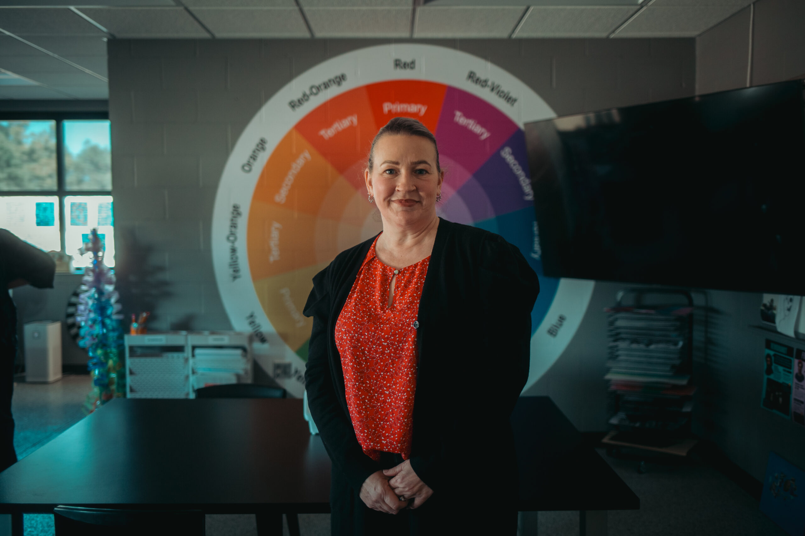 Roberta Ruud, Art Educator at McCrossan Boys Ranch, stands proudly in front of a color wheel painted on the wall of her art classroom.